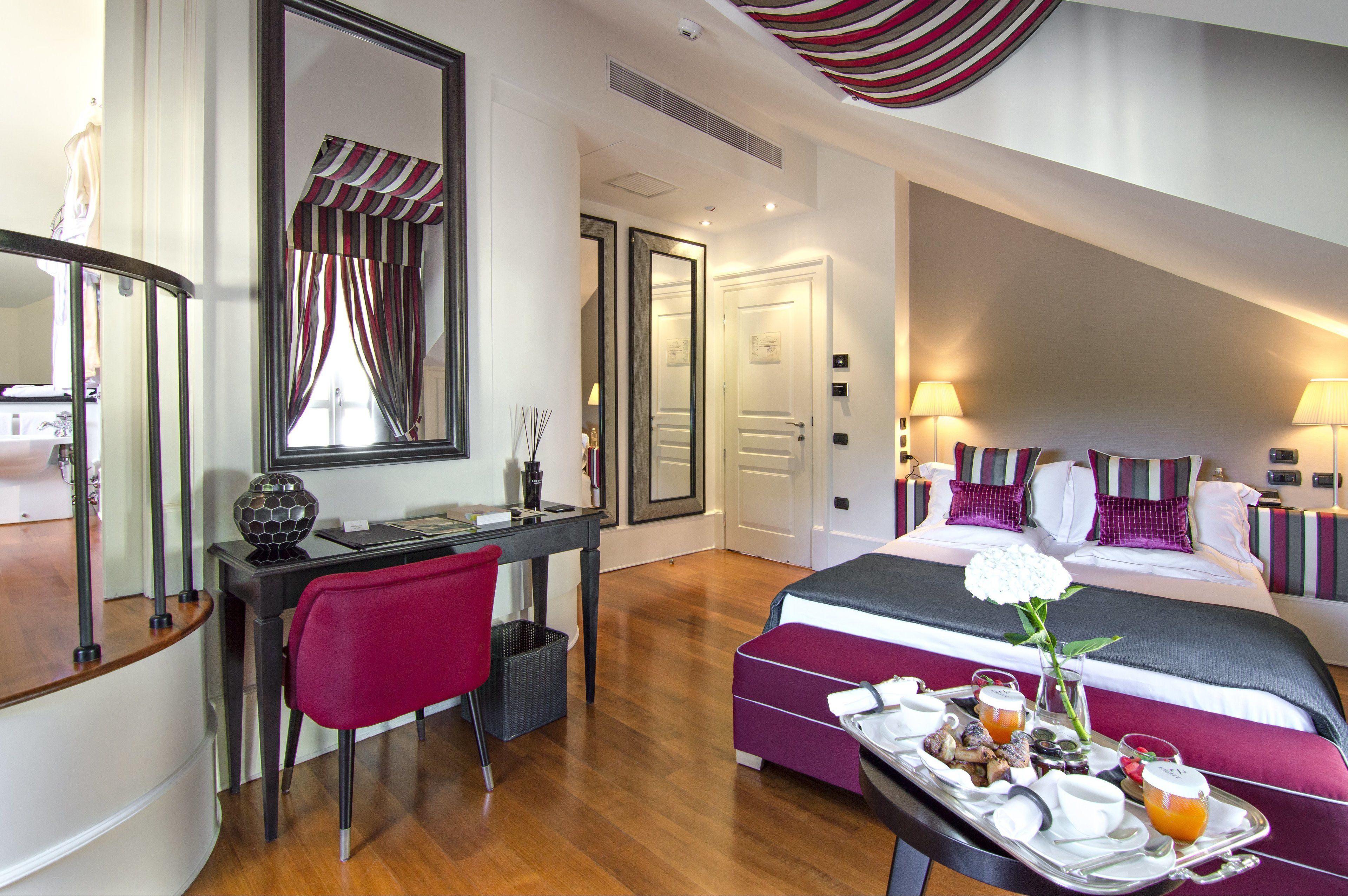 A hotel room with a bed, a desk, a chair, and a tray with breakfast items.