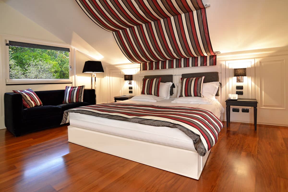 Ein Schlafzimmer mit einem großen Bett, einer schwarzen Couch und einem Fenster mit Blick auf Grünflächen.