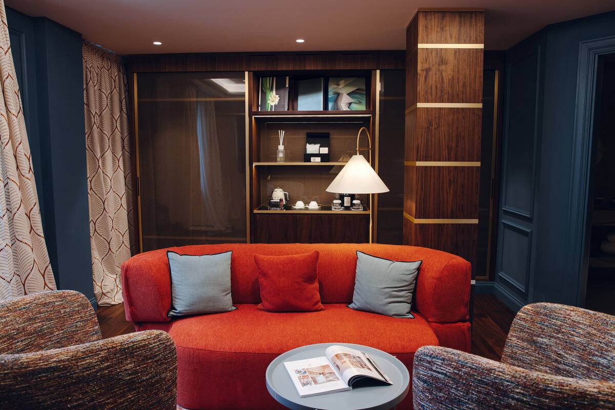 Ein modernes Wohnzimmer mit einem roten Sofa, zwei Sesseln, einem runden Couchtisch und einem Bücherregal mit Dekorationselementen.