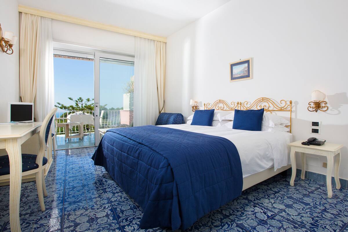 A hotel room with a bed, a desk, a chair, and a balcony with a view.