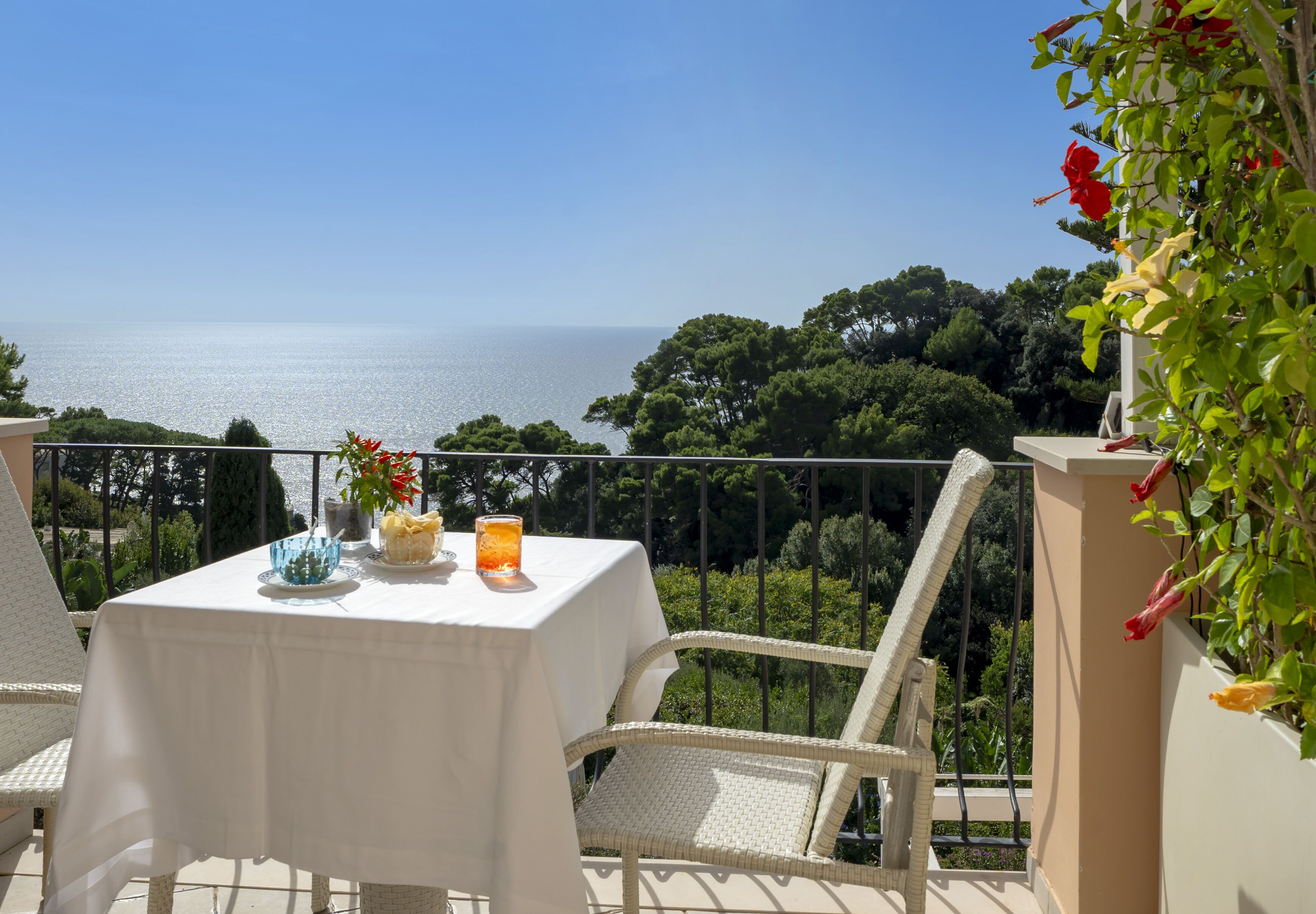 Ein Balkon mit Tisch für zwei Personen, mit Blick auf eine schöne Landschaft aus Meer und Grünflächen.