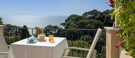 Ein Balkon mit Tisch für zwei Personen, mit Blick auf eine schöne Landschaft aus Meer und Grünflächen.