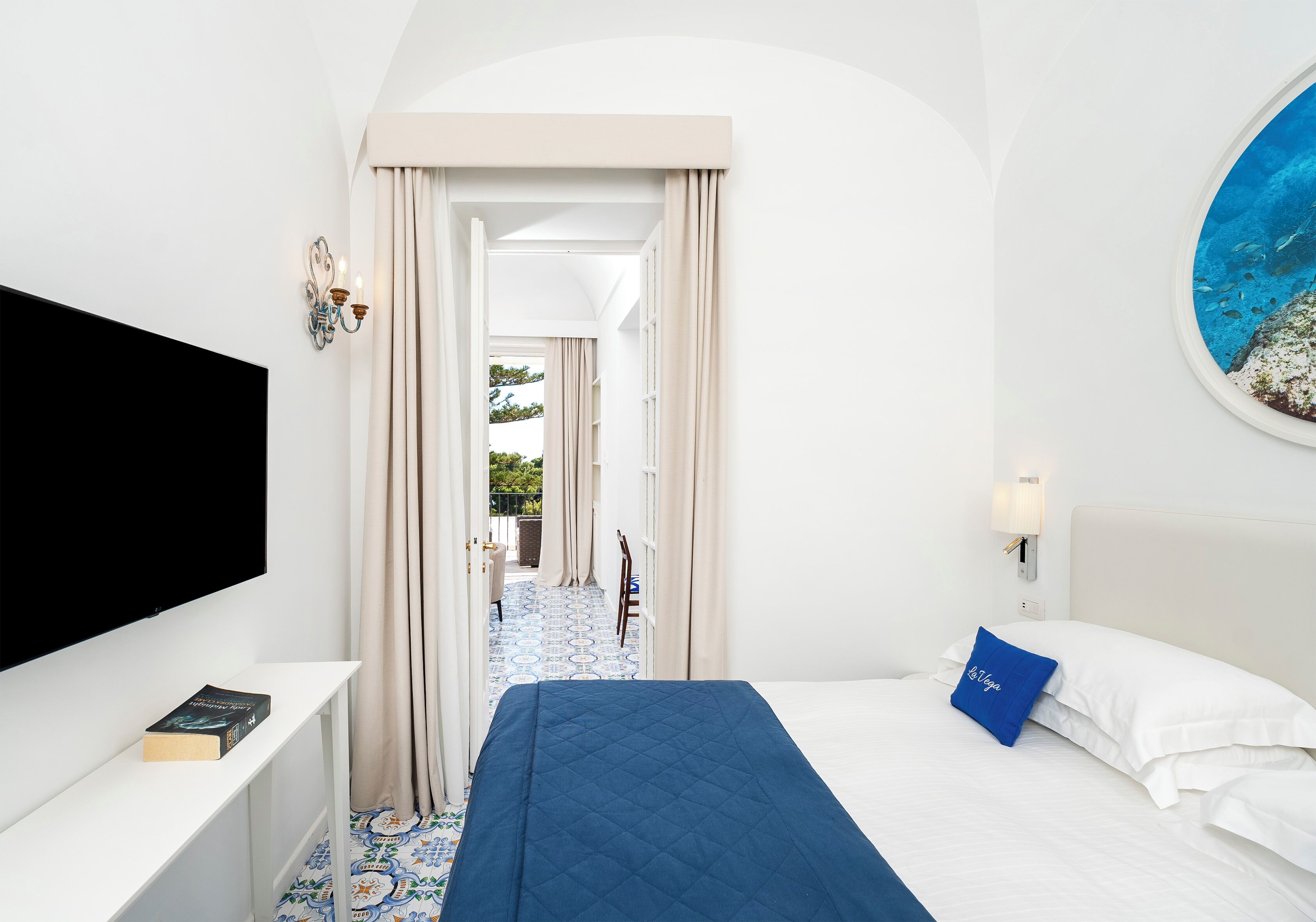 A hotel room with a bed, a TV, a desk, and a view of the outdoors.