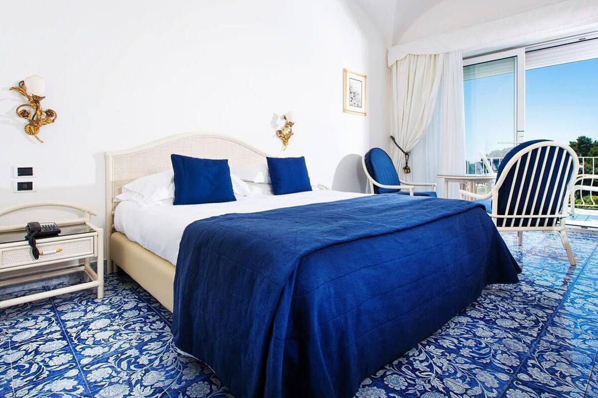 A hotel room with a bed, a nightstand, a chair, and a view of the outdoors.