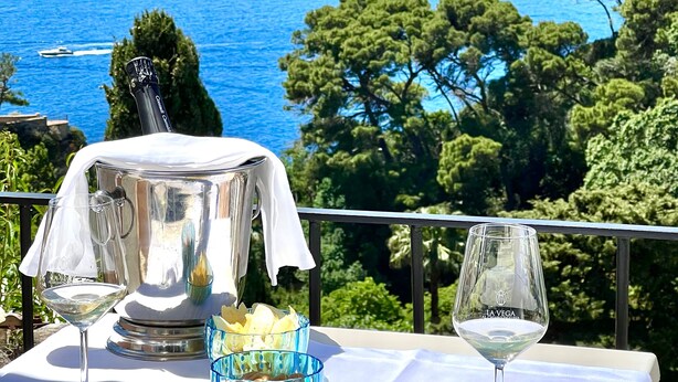 A table with a white tablecloth, two wine glasses, a bowl of snacks, and a bottle of champagne on a balcony overlooking the sea. - Hotel La Vega (Capri)
