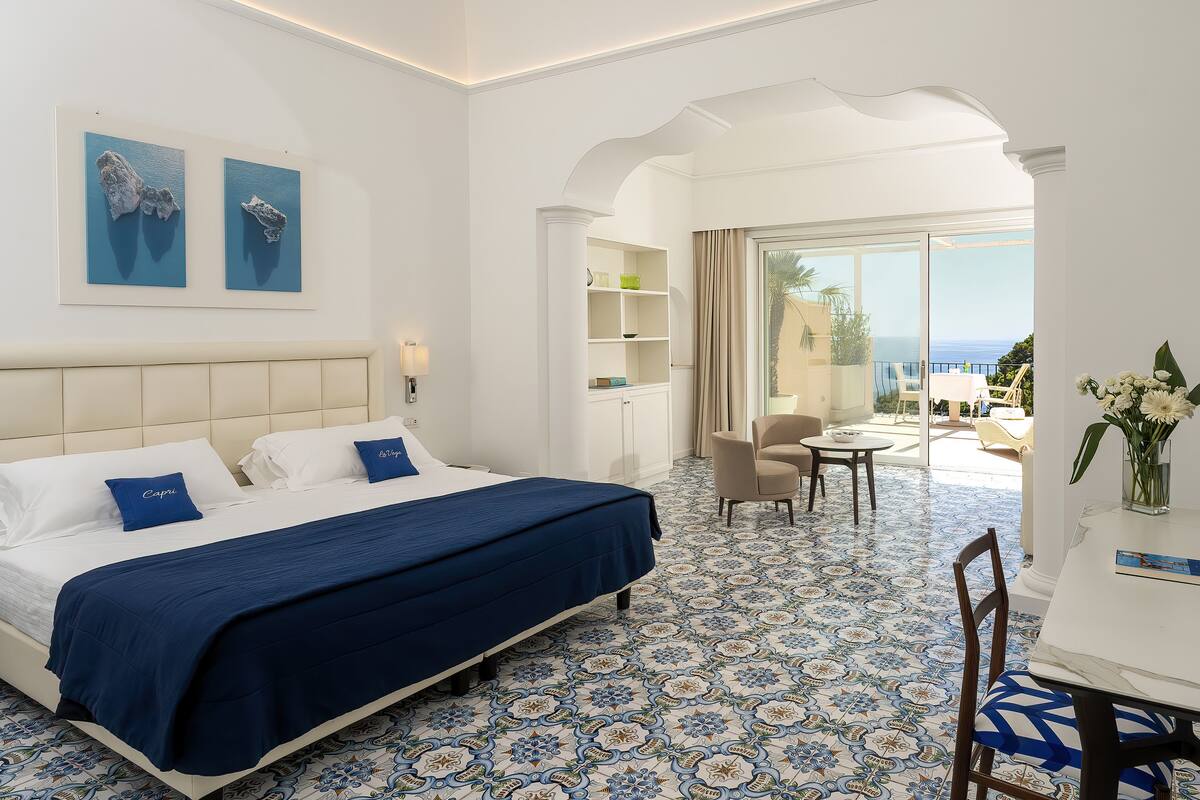 A hotel room with a bed, a desk, and a view of the sea.