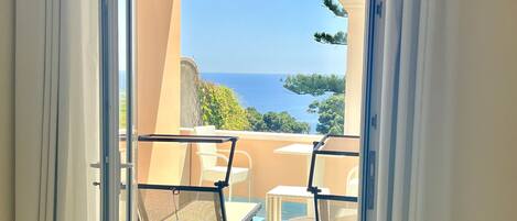 A balcony with a glass door, white curtains, and a view of the sea.