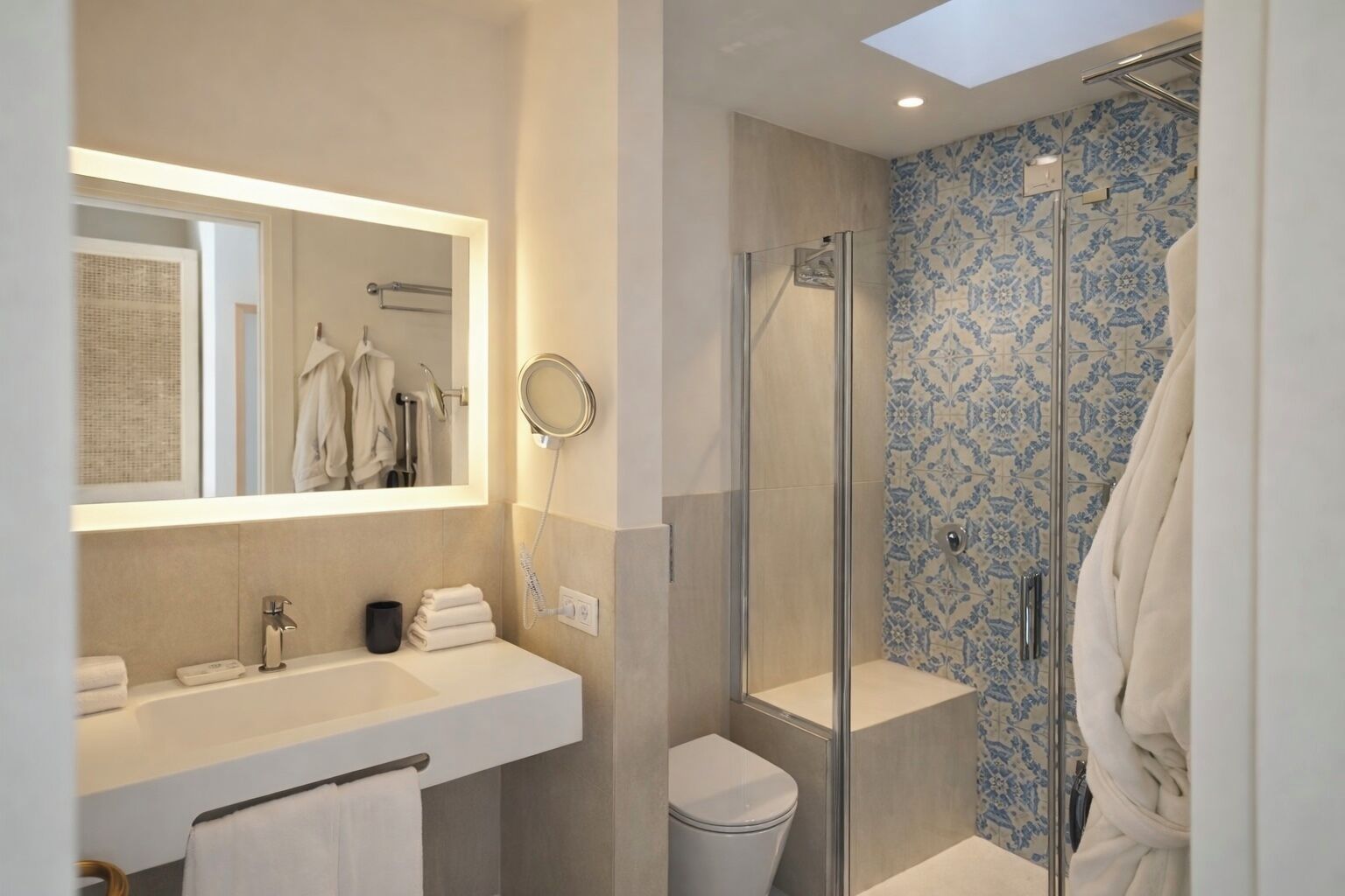Un baño moderno con ducha envuelta en vidrio, un espejo grande y un lavabo con toallero.