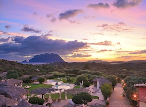 Un resort con piscina, zona de estar al aire libre y vistas a las montañas y al mar al atardecer.
