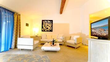 A well-lit living room with a sofa set, a coffee table with a bottle and fruit, and a television on a cabinet.