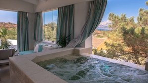 A spa area with a hot tub, large windows, and a view of trees and mountains. - Hotel Ollastu (Olbia)