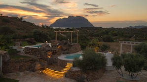 A resort with a swimming pool, stone structures, and a view of a mountain at sunset. - Hotel Ollastu (Olbia)