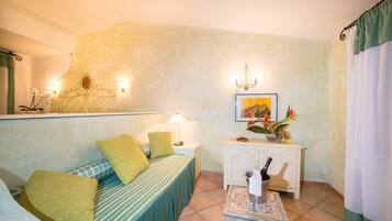 A cozy room with a bed, a small table with a bottle, and a wall-mounted shelf with decorative items.