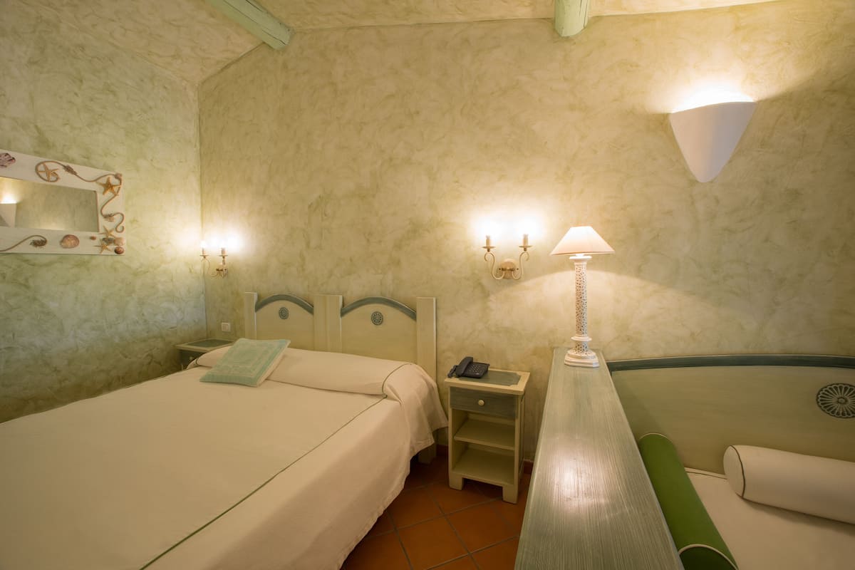 A hotel room with a bed, bedside table, lamp, and a small desk with a telephone.