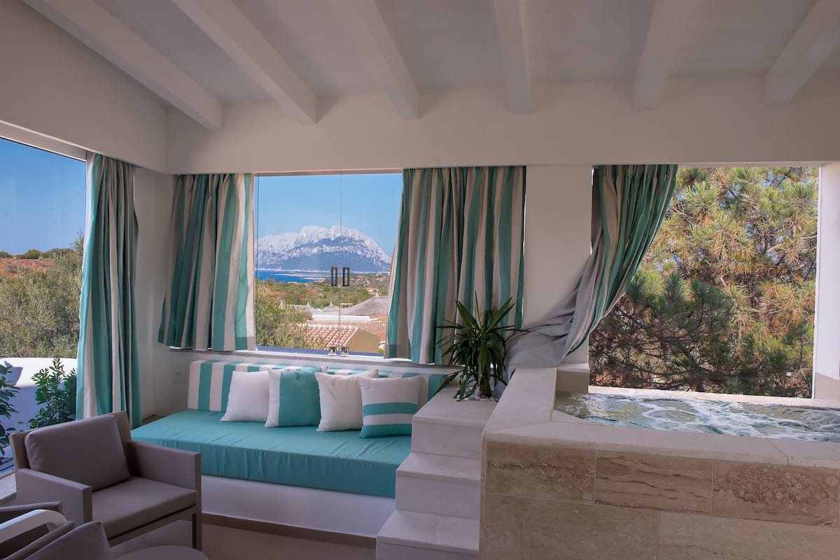 A bedroom with a bed, a bathtub, and a view of a mountain and trees.
