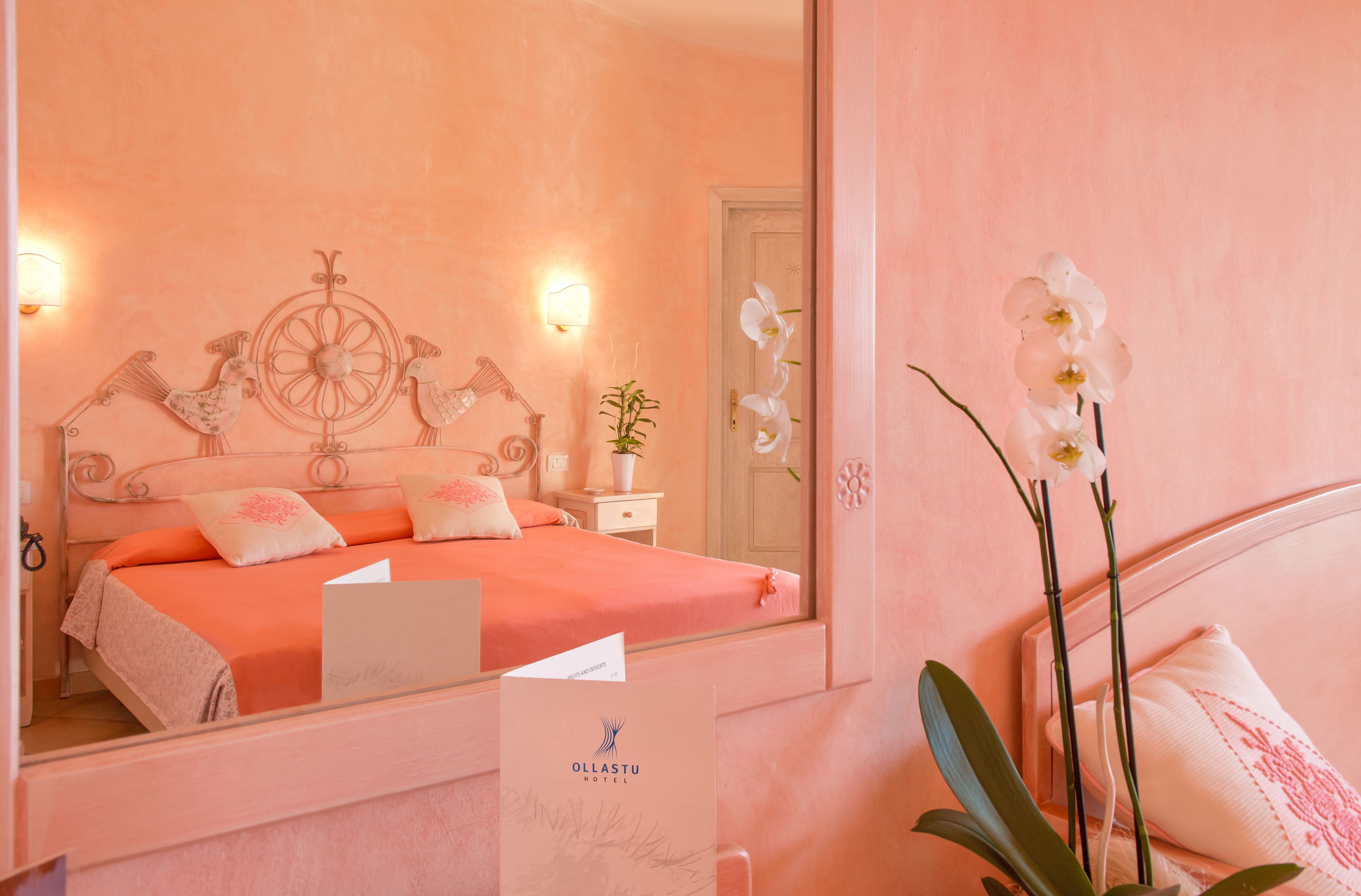 Una habitación de hotel con cama, mesita de noche, espejo y un cartel del Hotel Ollastu.
