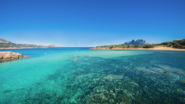 A coastal landscape with clear turquoise waters, rocky shorelines, and distant mountains. - Hotel Ollastu (Olbia)