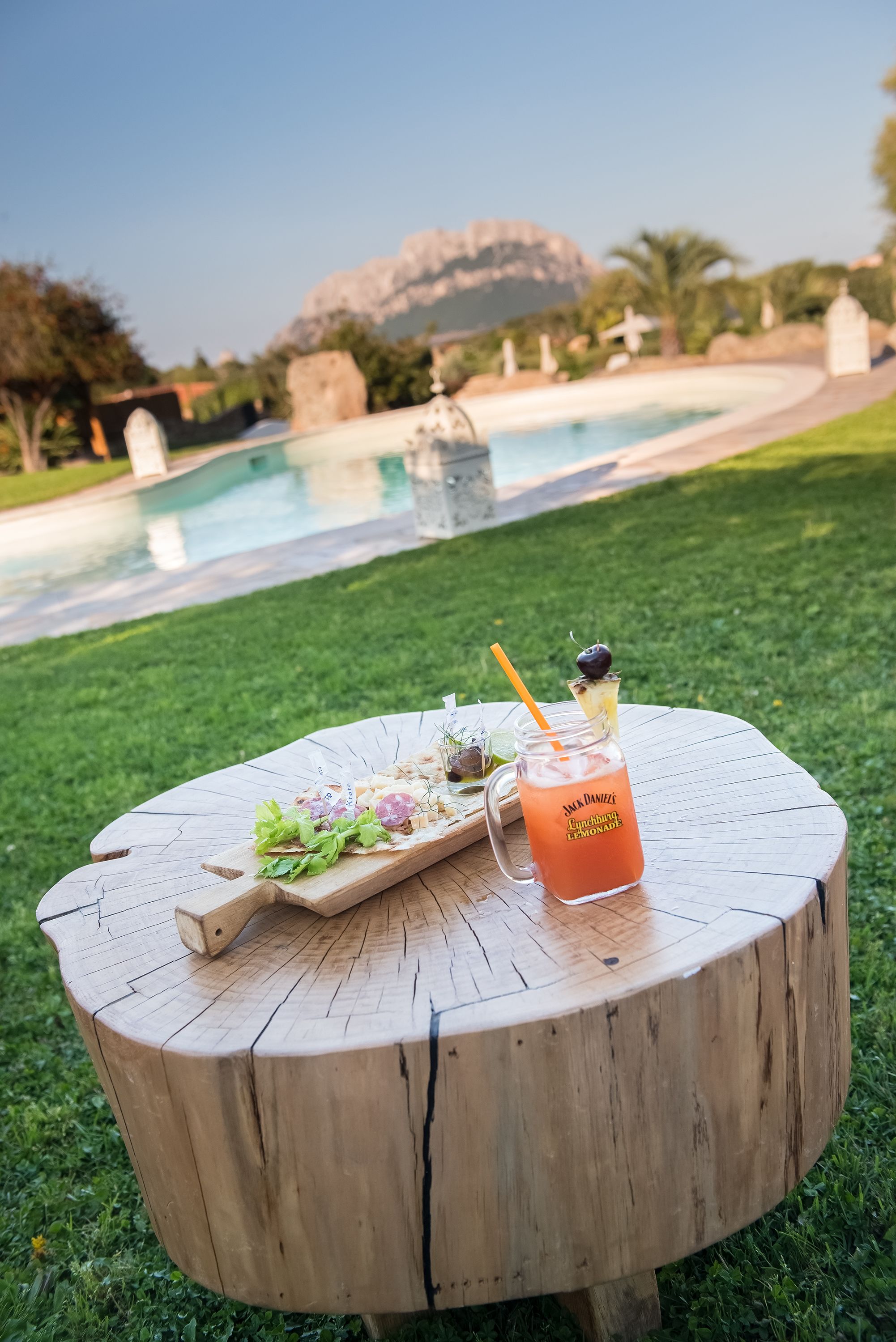 A wooden table with a salad and a drink in front of a pool.