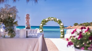 A beach wedding setup with a floral arch and a table set for guests. - Hotel Ollastu (Olbia)