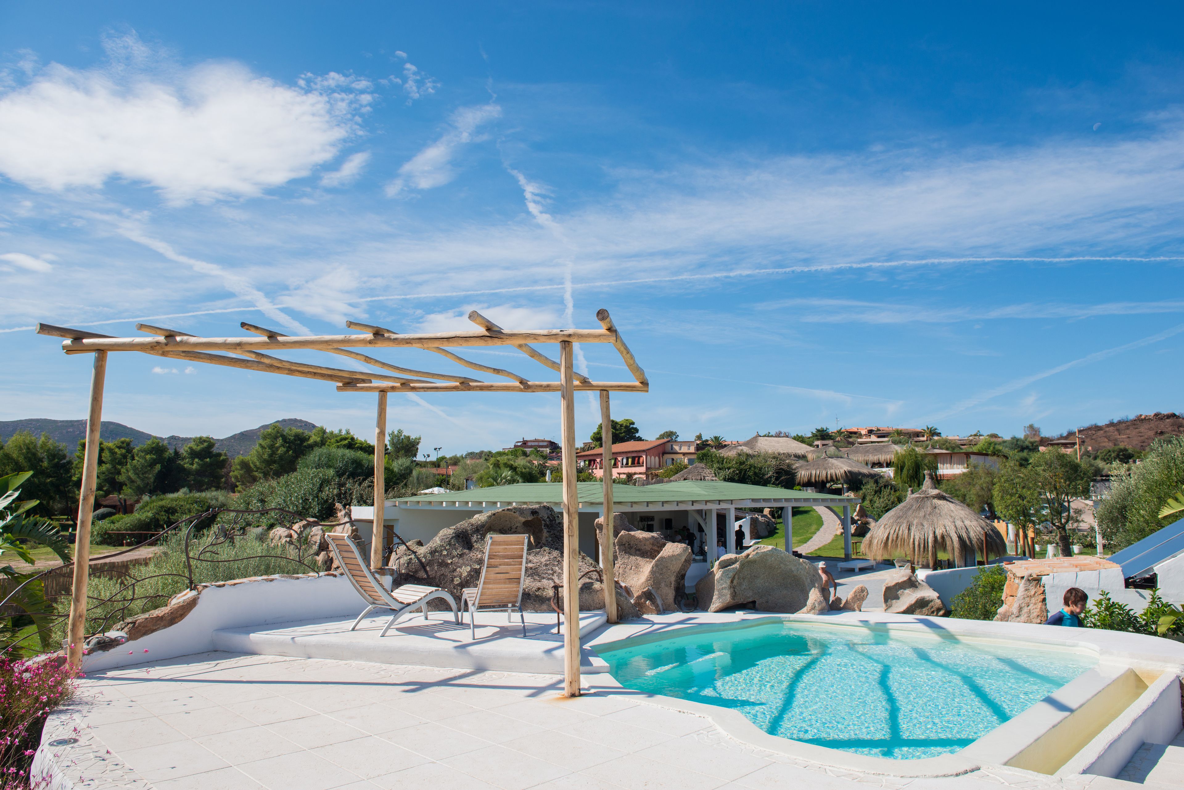 A pool area with a pergola, lounge chairs, and a view of the surrounding landscape.