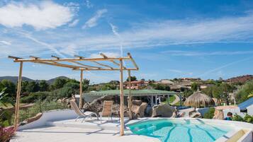 A pool area with a pergola, lounge chairs, and a view of the surrounding landscape.
