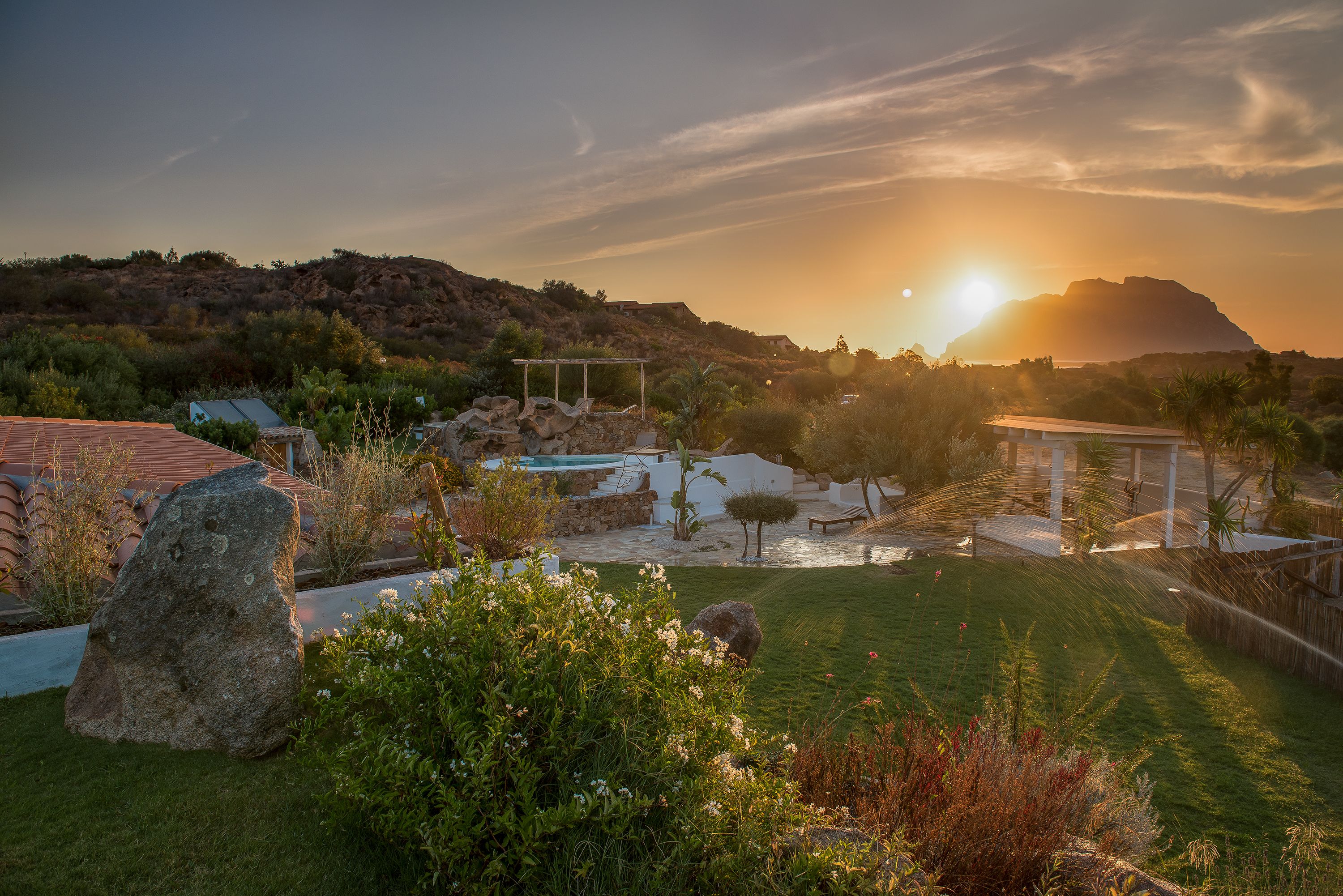 Ein angelegter Garten mit Pool, einer Pergola und Blick auf einen Berg bei Sonnenuntergang.