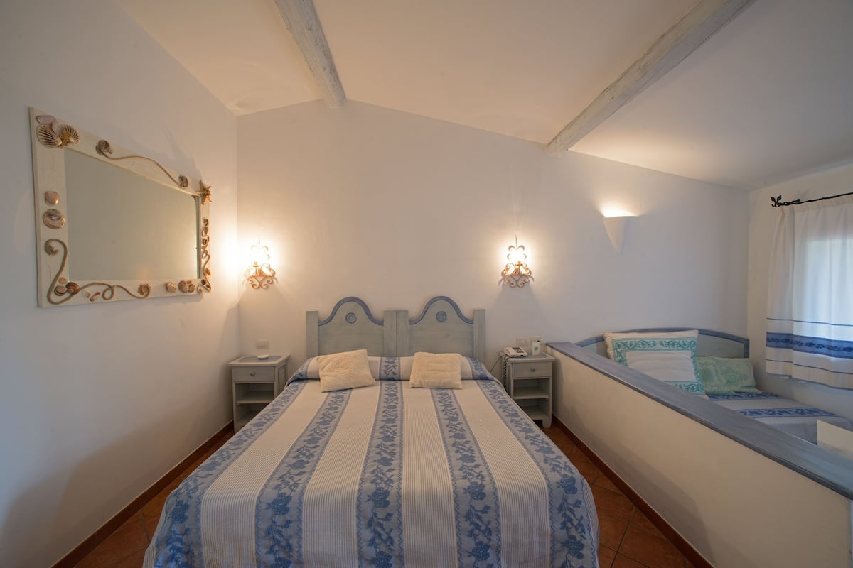 A bedroom with a large bed, two bedside tables, a nightstand, a mirror, and a window with curtains.