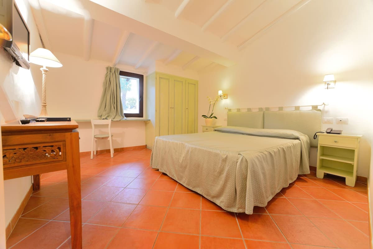 A bedroom with a bed, a desk, a chair, and a window.