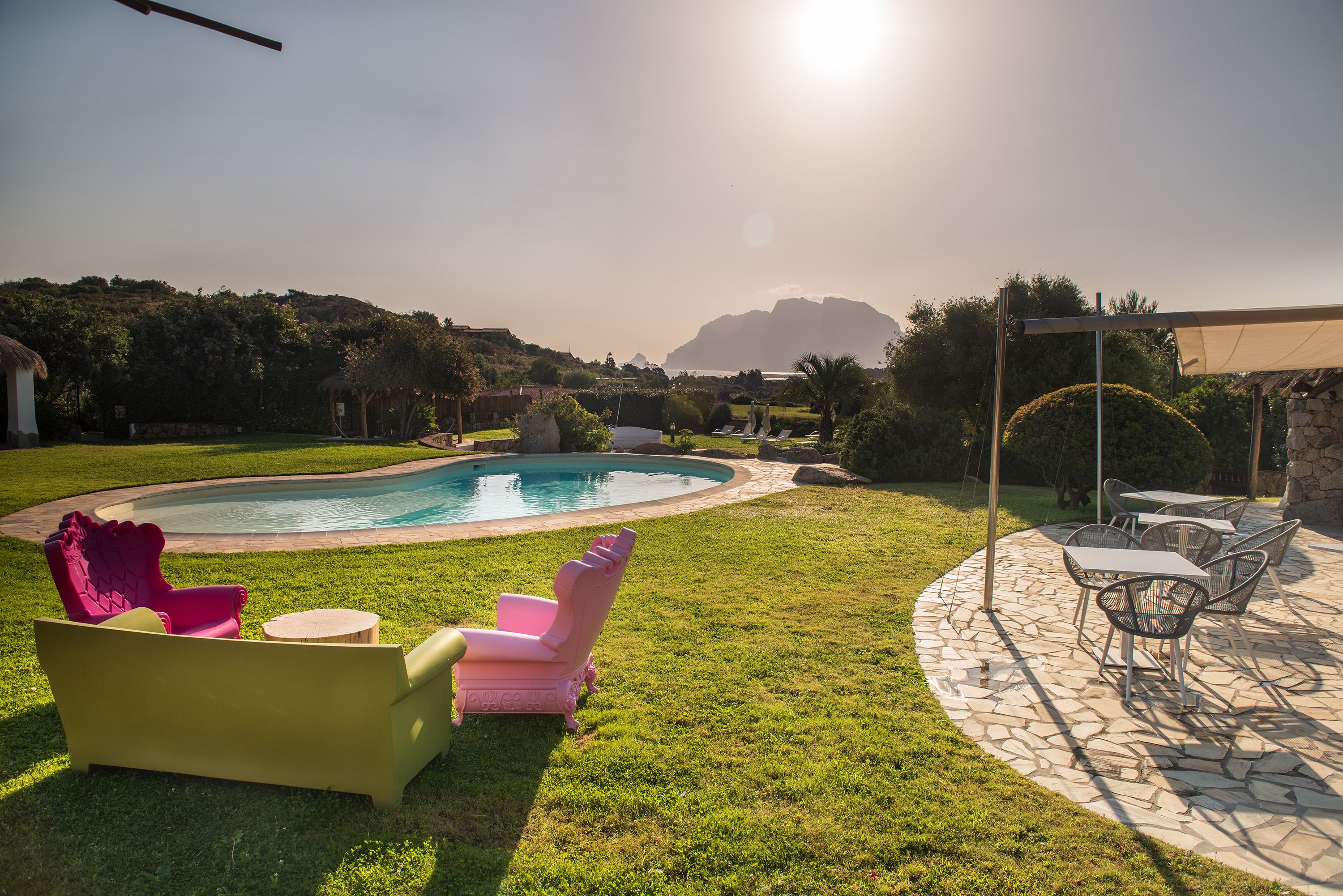 Ein Garten mit Pool, einer Terrasse mit Stühlen und Tischen sowie Blick auf einen Berg.