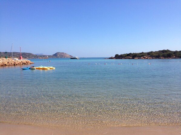 A beach with clear water, boats, and a rocky shoreline. - Hotel Ollastu (Olbia)