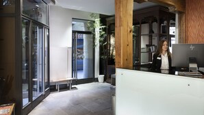 Zona de recepción con recepcionista, techo de madera, puerta de vidrio y un banco.