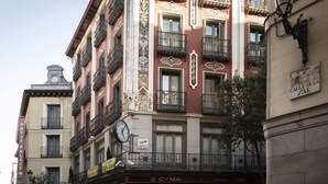 Un edificio de varios pisos con balcones, un reloj y varios letreros, incluyendo "POSADA DEL PEINE" y "CYMA".