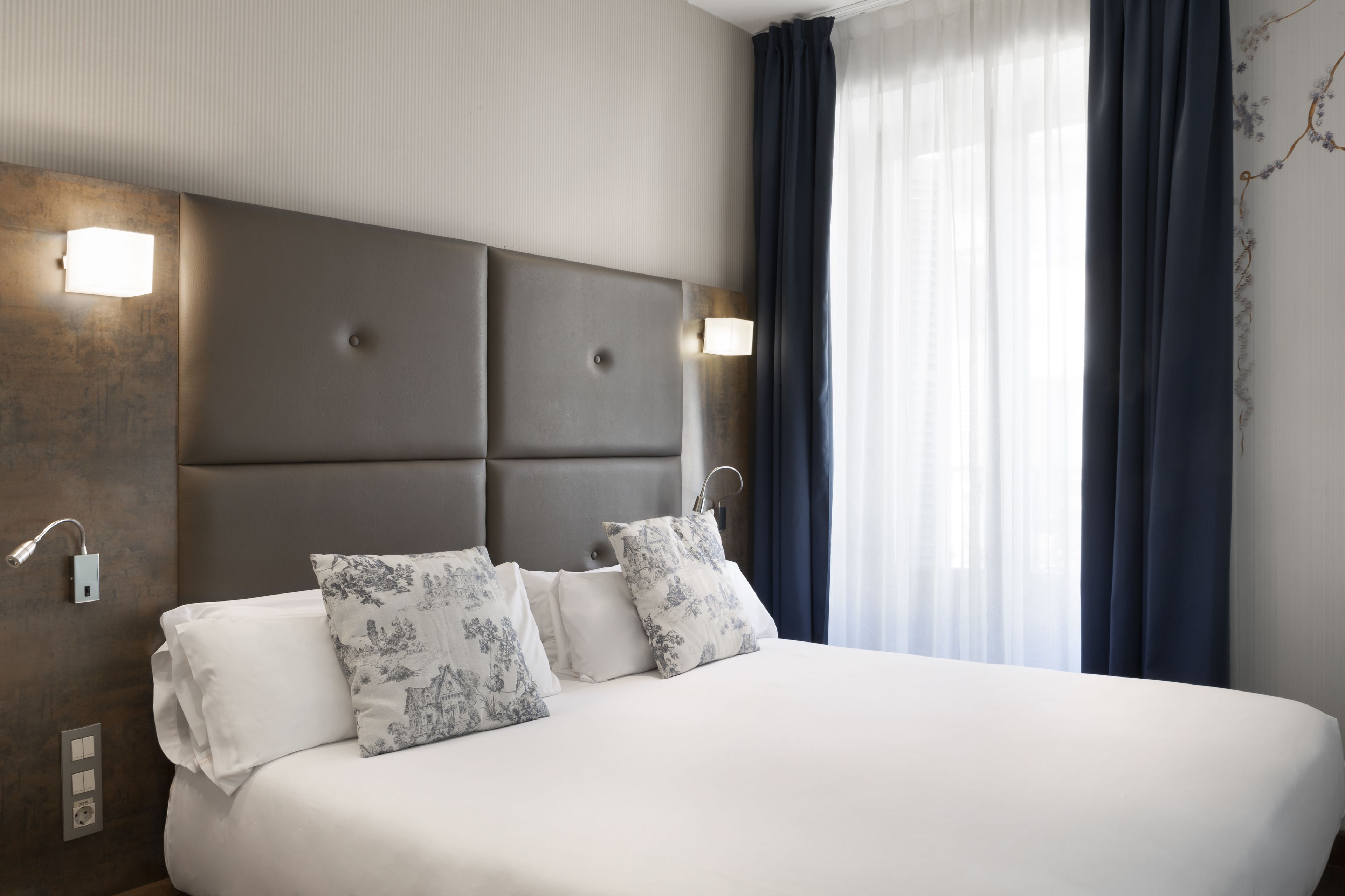 Habitación de hotel moderna con una cama grande, dos mesitas de noche y una lámpara de pared.