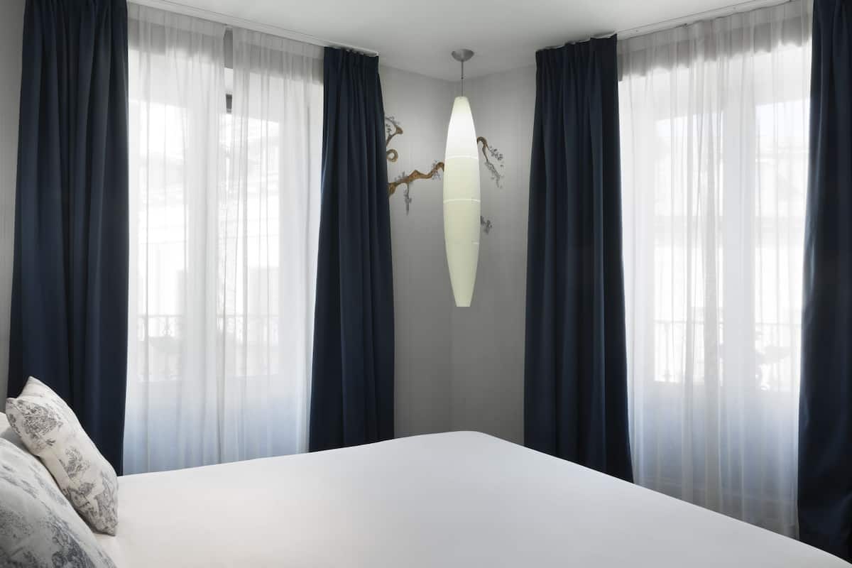 Une chambre à coucher avec un grand lit, des rideaux foncés et un luminaire fixé au mur.