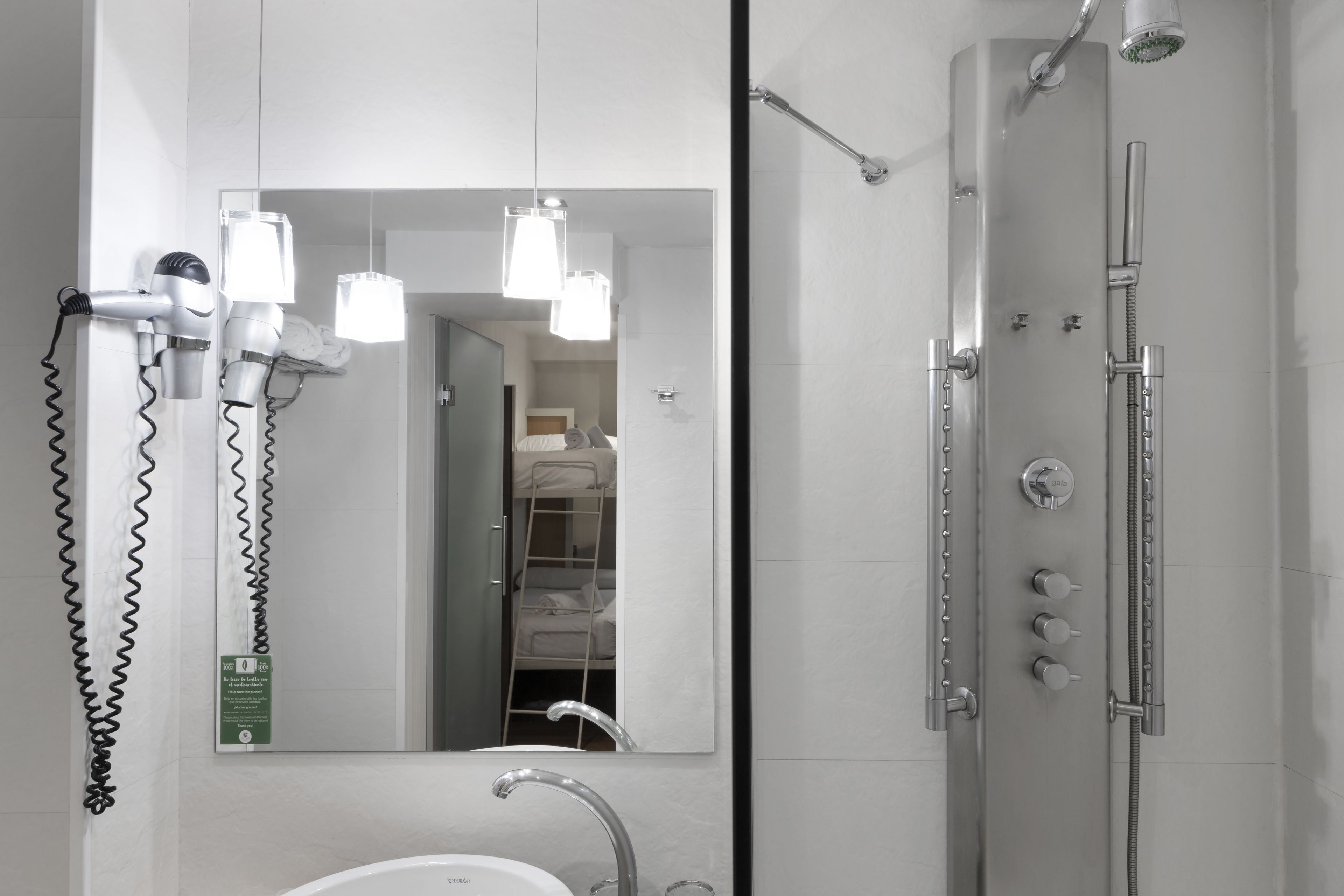 Un baño moderno con un espejo grande, un lavamanos, ducha con varios controles y secadores de pelo montados en la pared.