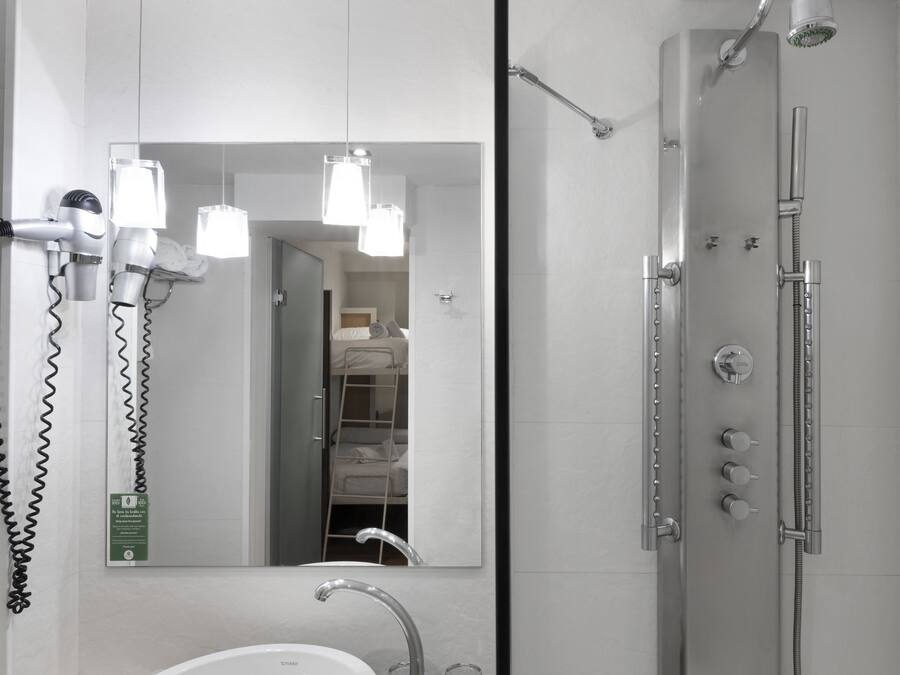 Un baño moderno con un espejo grande, un lavamanos, ducha con varios controles y secadores de pelo montados en la pared.