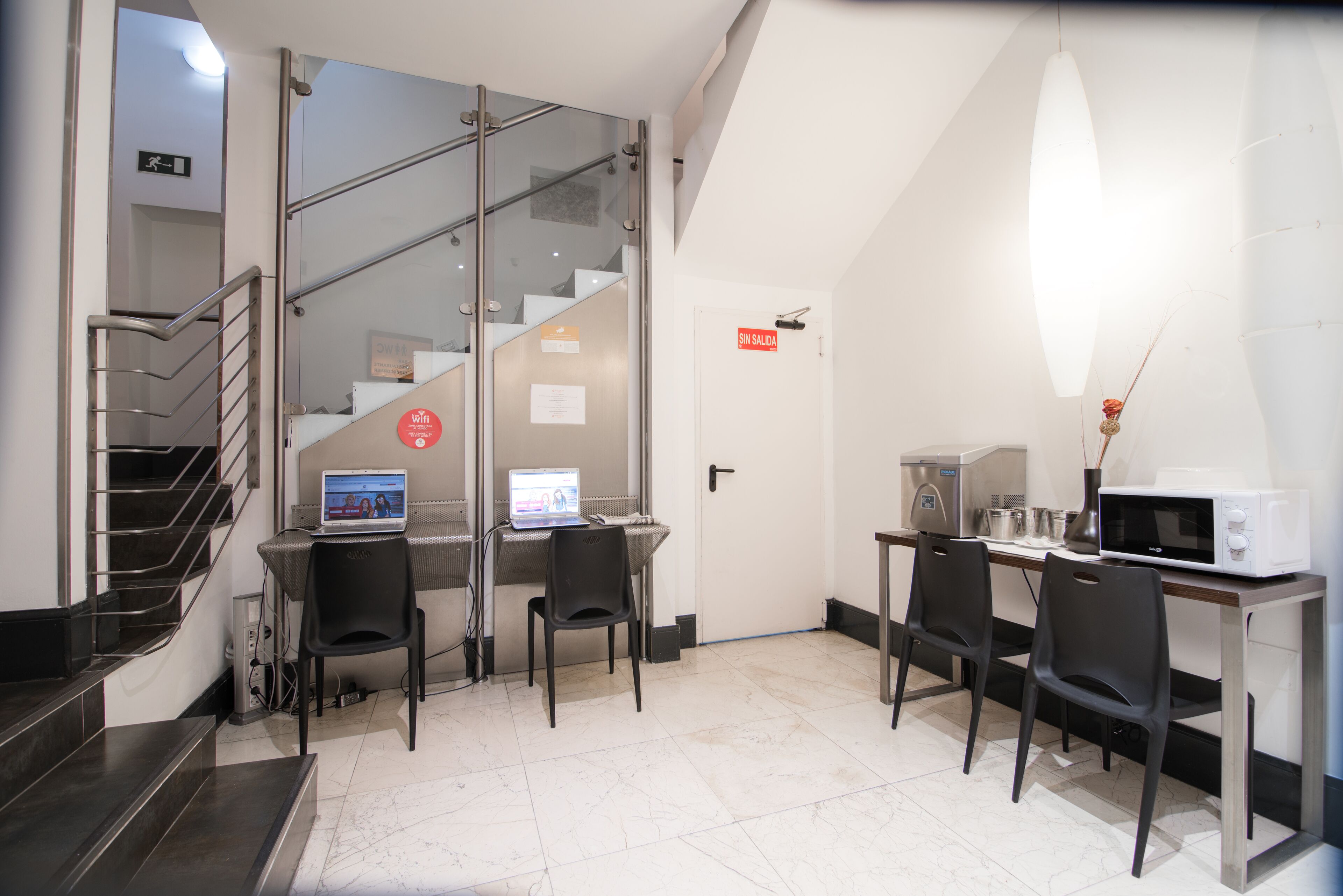 Een moderne hotelkamer met een trap, een bureau met twee computers, een magnetron en een zithoek met stoelen.