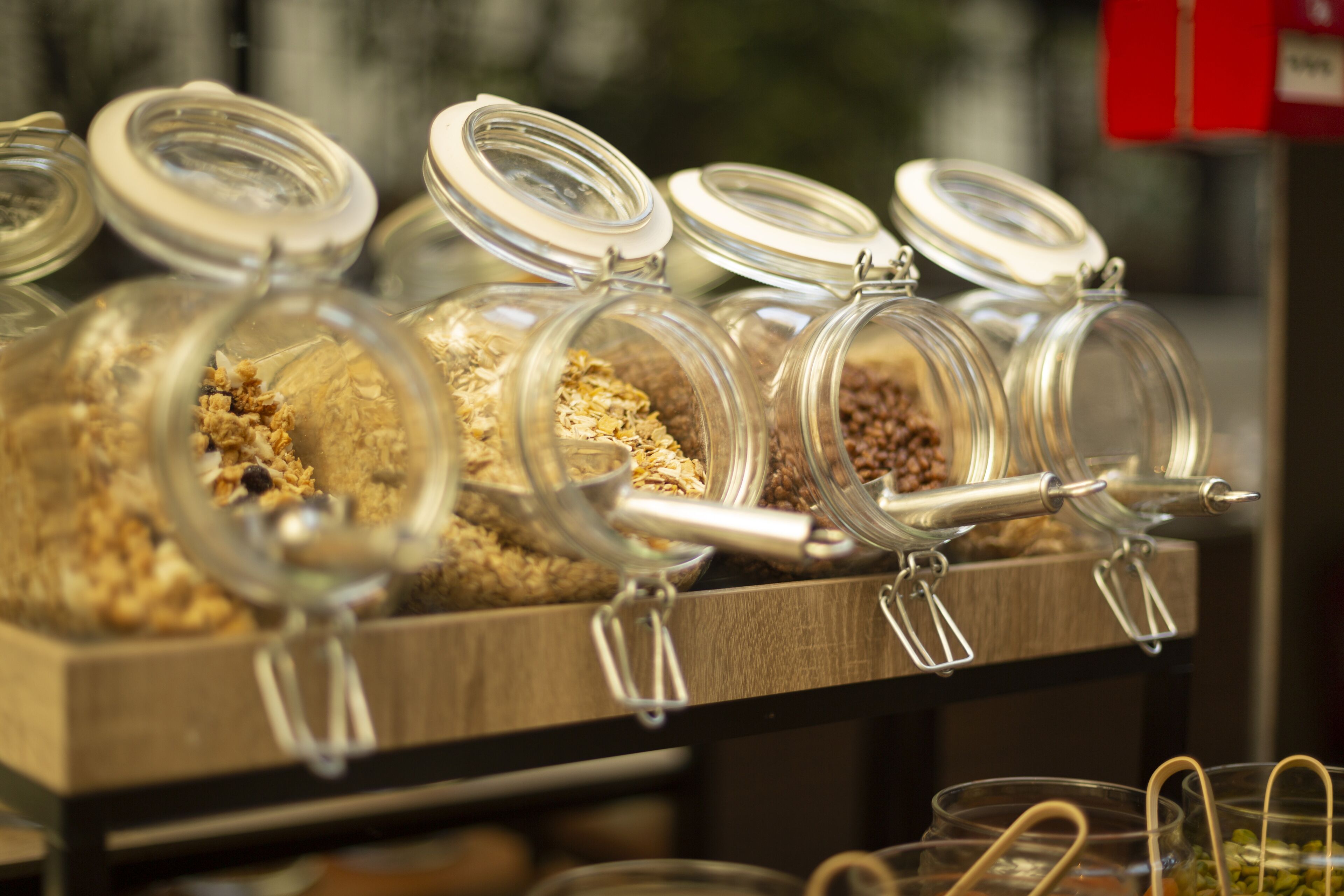 Una exposición de diversos alimentos en frascos de vidrio con tapas metálicas, dispuestos en un estante de madera.