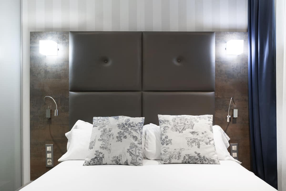 Une chambre à coucher moderne avec un grand lit, deux tables de chevet et une tête de lit dotée d’un éclairage intégré.