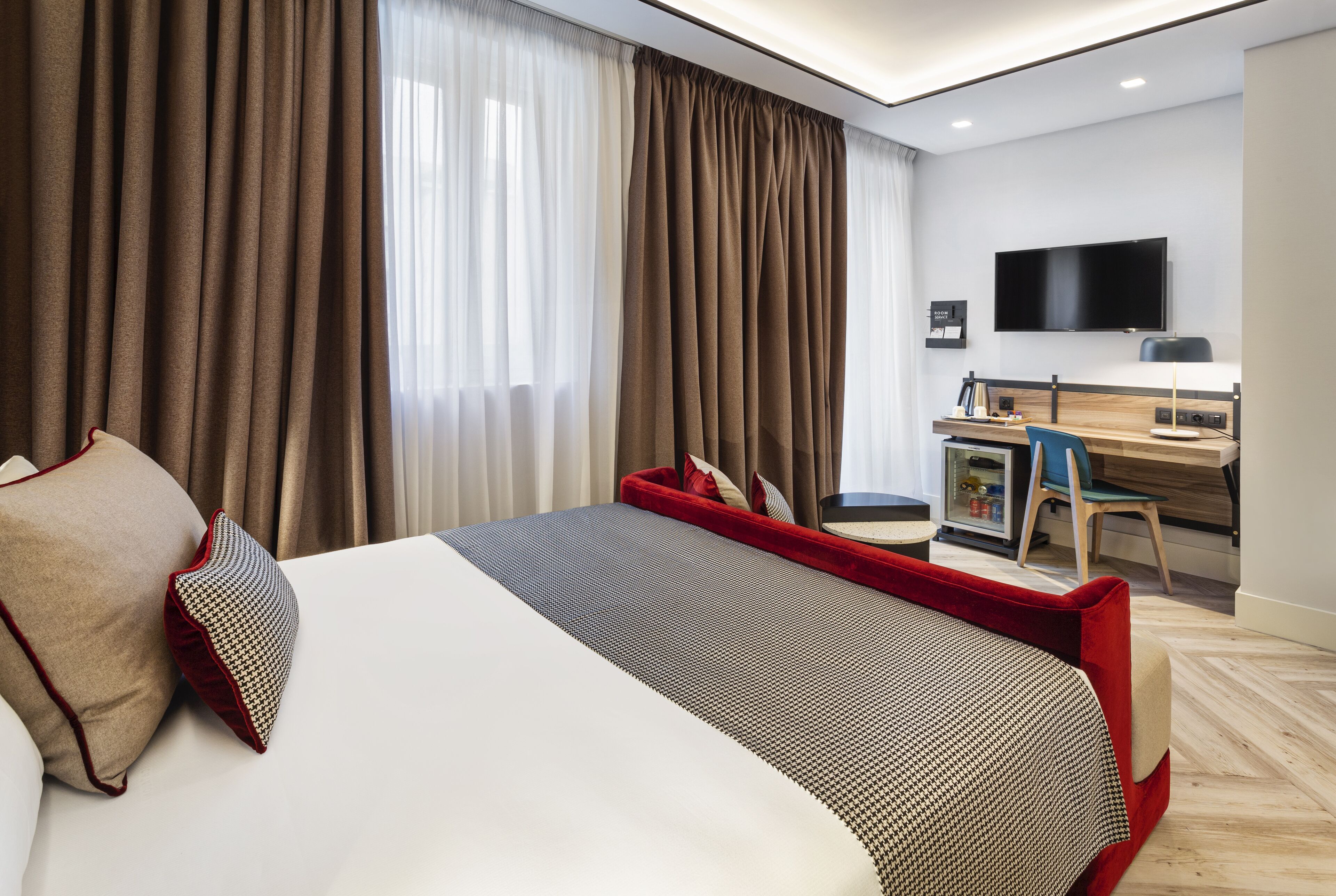 A hotel room with a bed, a desk, a chair, a TV, and curtains.