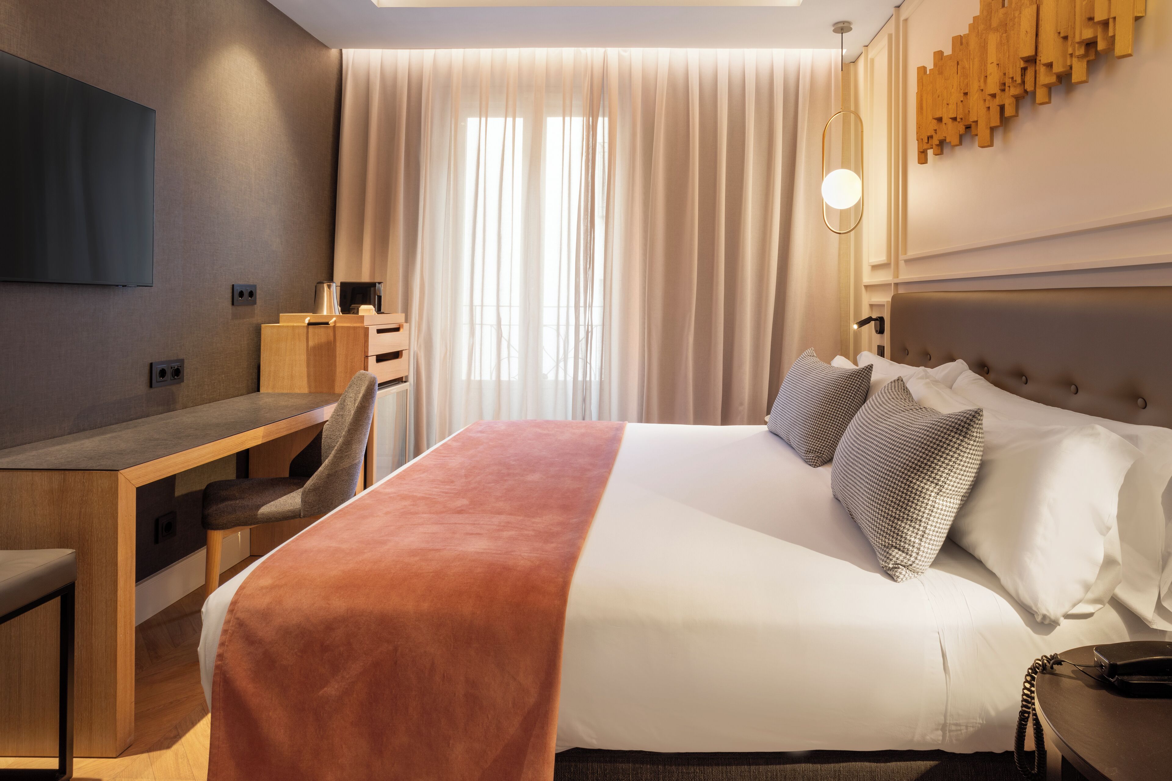 A hotel room with a bed, a desk, a chair, a TV, and a large window with curtains.