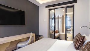 Una habitación de hotel moderna con una cama grande, un televisor de pantalla plana en la pared, un escritorio con silla y una puerta corrediza de vidrio que da a un balcón.
