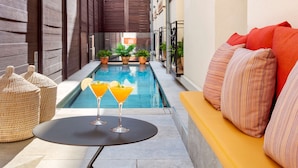 Un área junto a la piscina con un sofá amarillo, dos bebidas sobre una mesa y plantas en macetas.