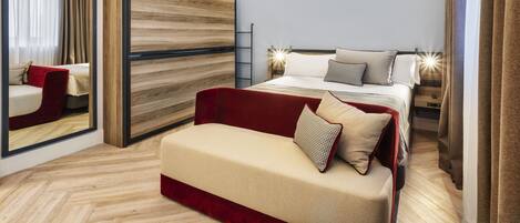 A modern hotel room with a large bed, a red sofa, a wooden accent wall, and a mirror.