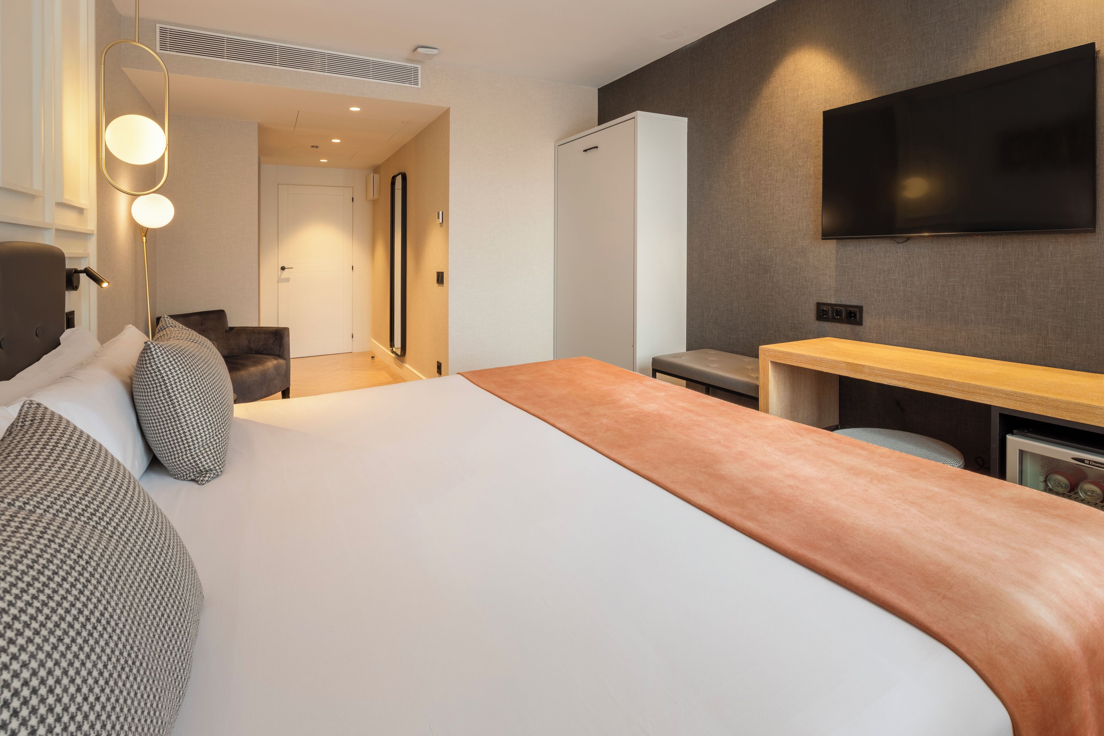 Una habitación de hotel moderna con una cama grande, un televisor de pantalla plana montado en la pared, un escritorio y una zona de estar con una silla y un sofá.