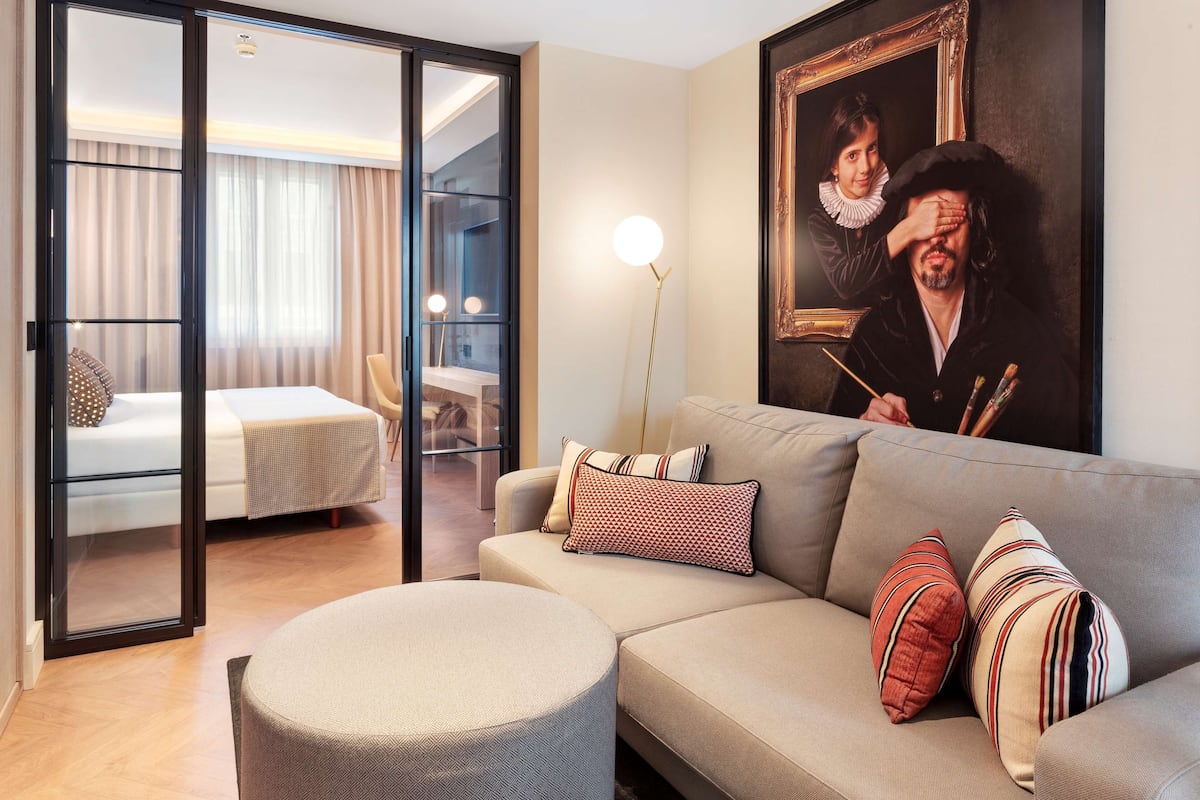 A modern hotel room with a sofa, ottoman, and a painting on the wall.