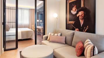Una habitación de hotel moderna con sofá, reposapiés y un cuadro en la pared.