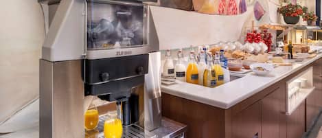 A buffet setup with a coffee machine, various food items, and a fruit display.
