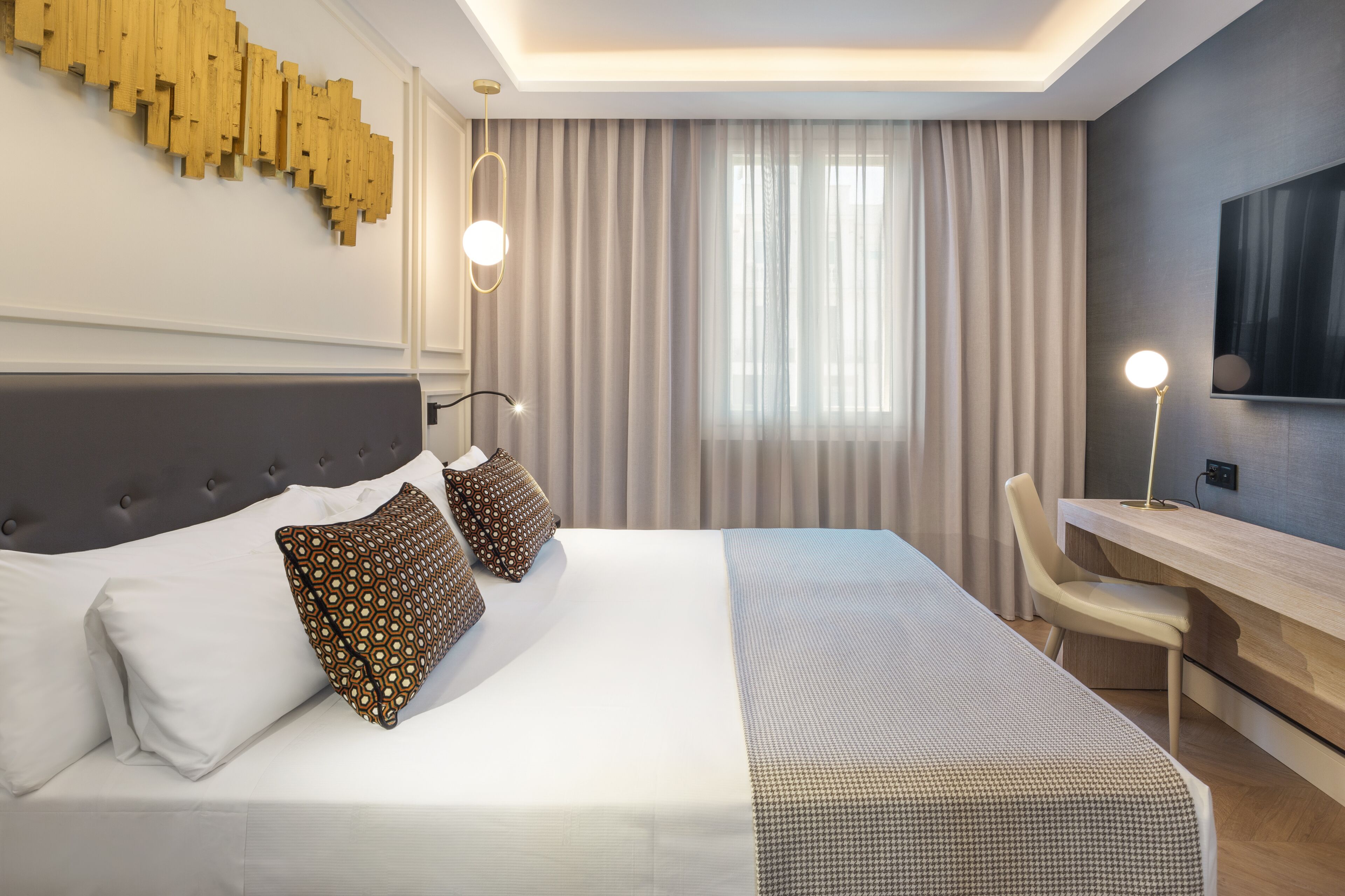 A modern hotel room with a large bed, a desk, and a TV.