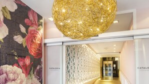 Entrada de hotel con una pared floral, una lámpara esférica y un felpudo negro.